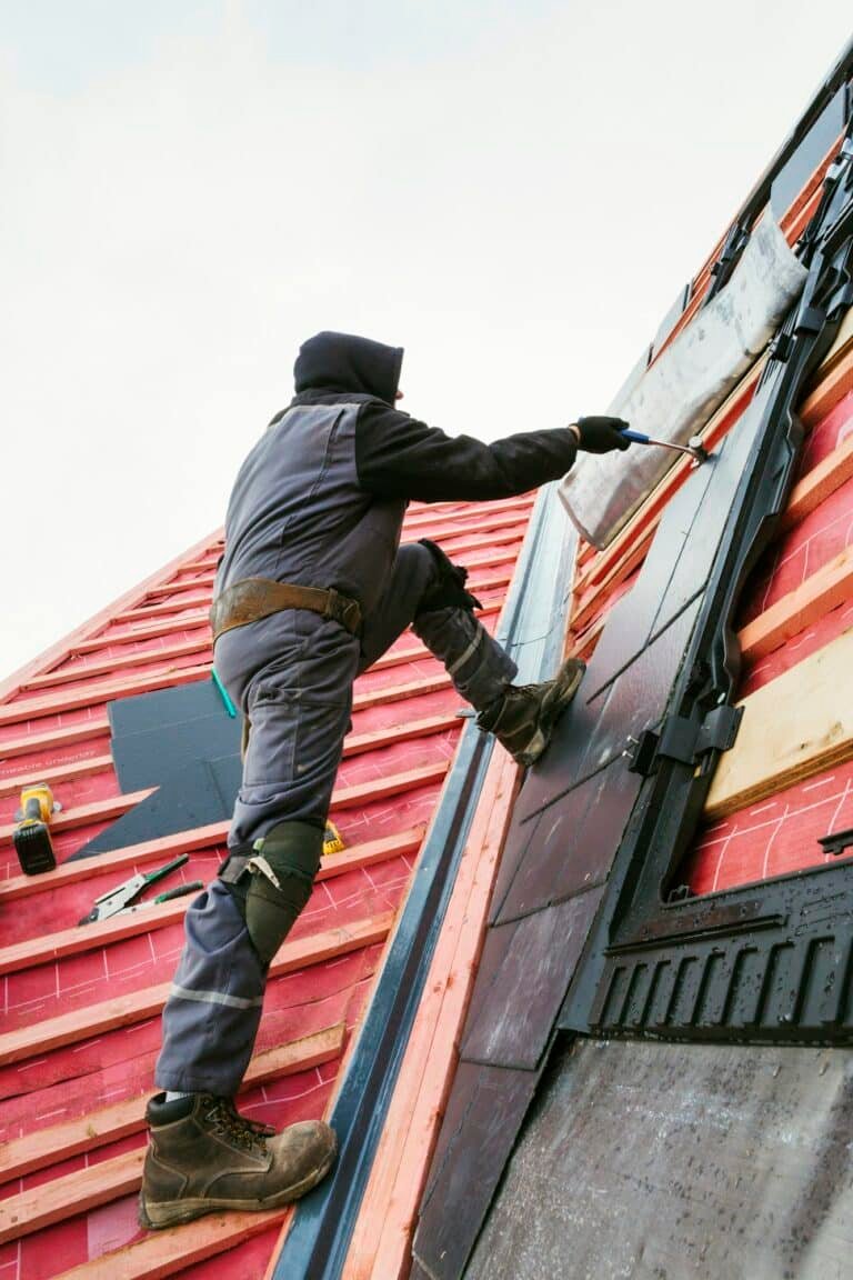 Travailleur installant des tuiles sur une toiture en pente.