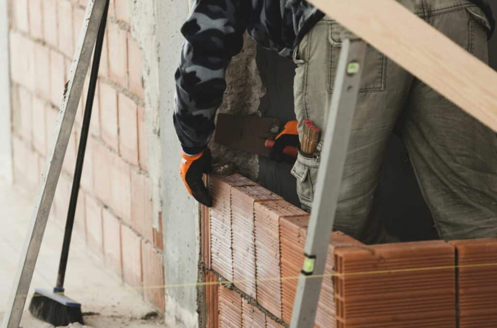 Travailleur construisant un mur en briques rouges.