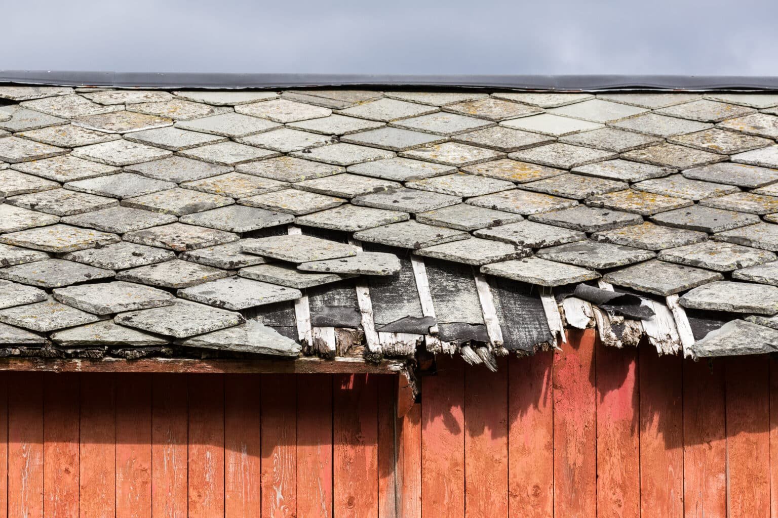 Toiture endommagée d'un vieux bâtiment en bois avec des tuiles cassées et une structure visible en mauvais état.