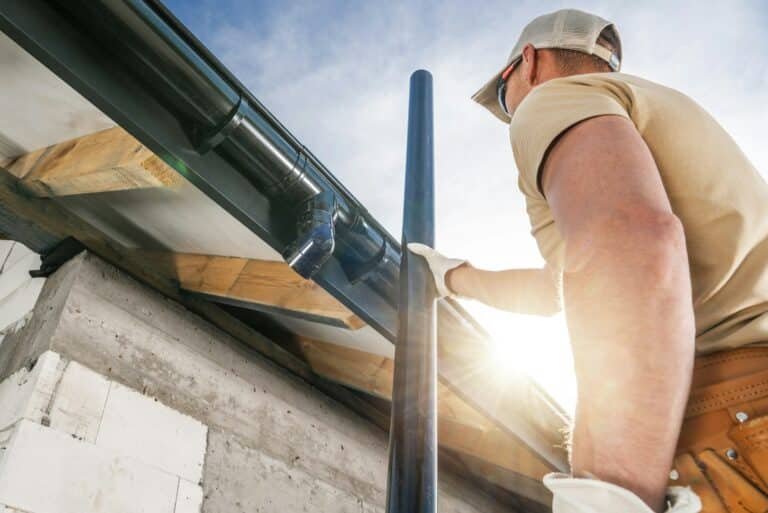 Travailleur installant une gouttière noire sur le bord d'une toiture d'une maison.