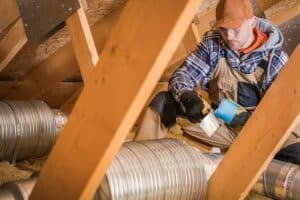 Ouvrier utilisant du ruban adhésif pour sceller un conduit de ventilation dans un grenier.