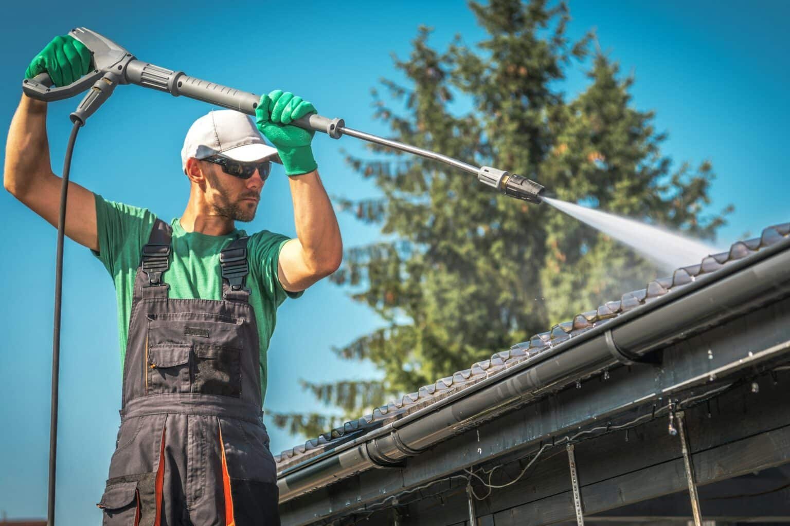 Homme utilisant un jet d'eau à haute pression pour nettoyer la toiture d'une maison.