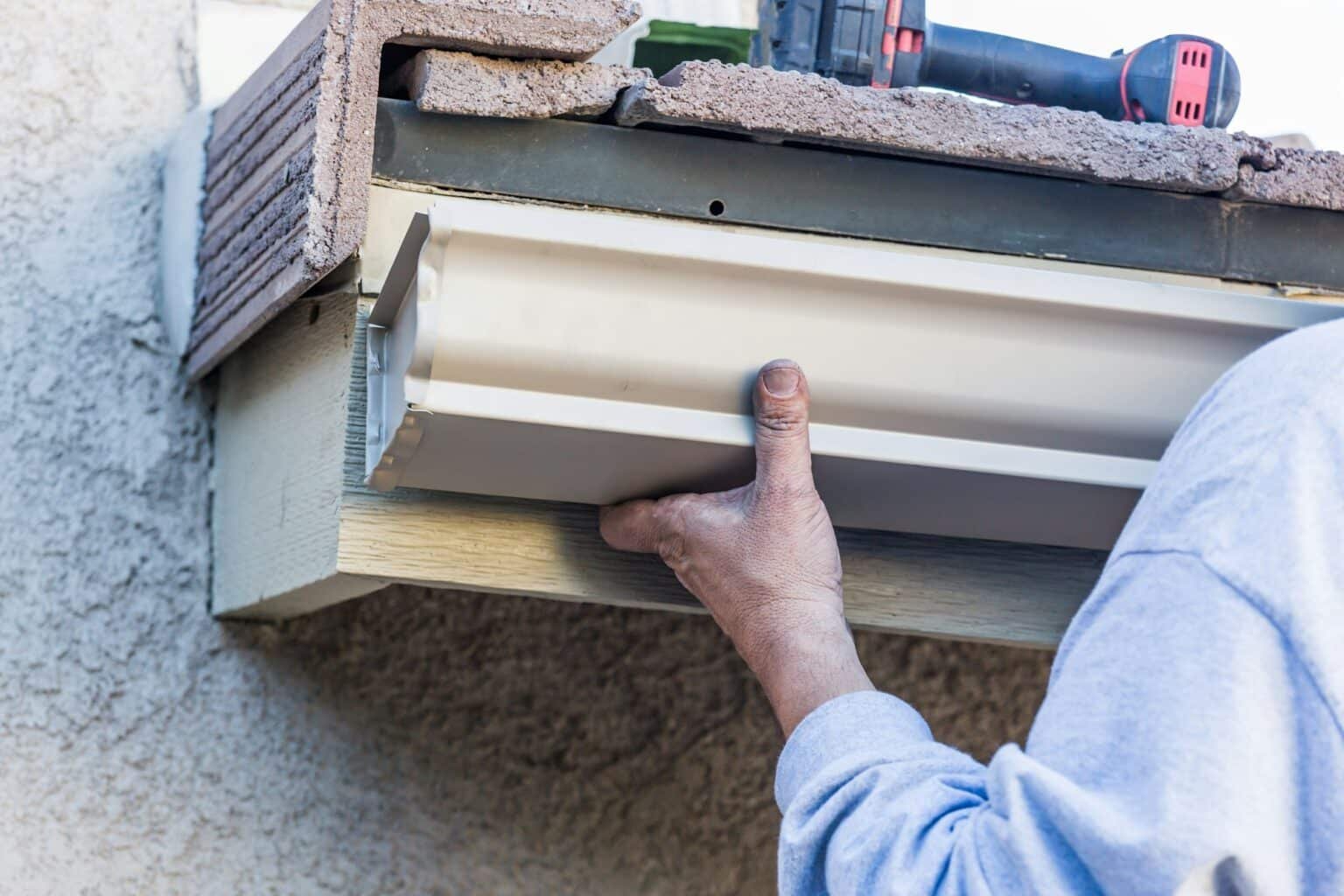 Travailleur installant une gouttière blanche sur le bord d'une toiture d'une maison.